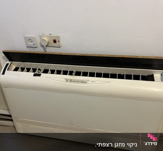 מזגן קיר לבן עם תריסים פתוחים ושקע חשמל